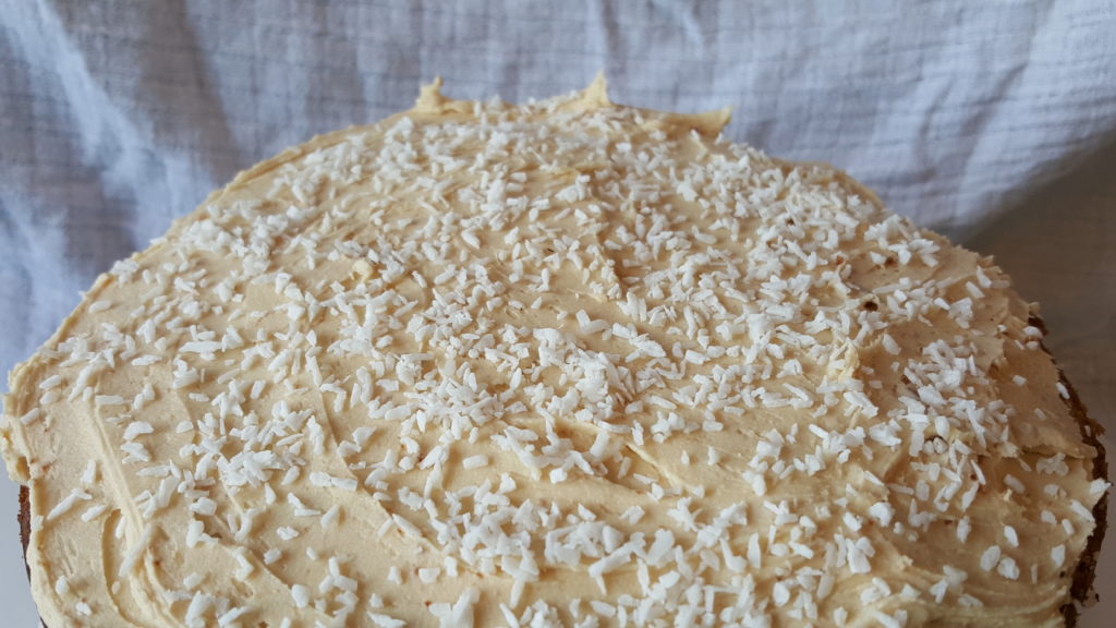 Coconut coffee triple layer cake topping with coffee butter icing and coconut flakes