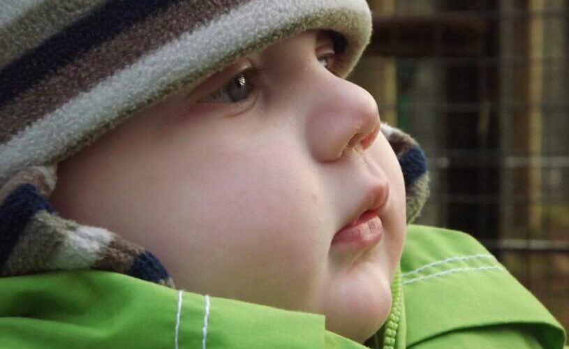 A close up of a baby's face, he is wearing a brown striped hat and a green coat