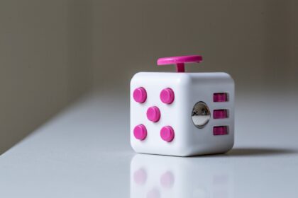 A white and purple fidget cube on a flat shiny surface in the foreground; 5 Conditions Fidget Cubes Could Help Treat