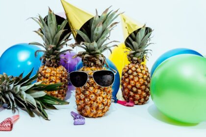 Pineapple wearing a party hat and sunglasses. Balloons. Children's party.