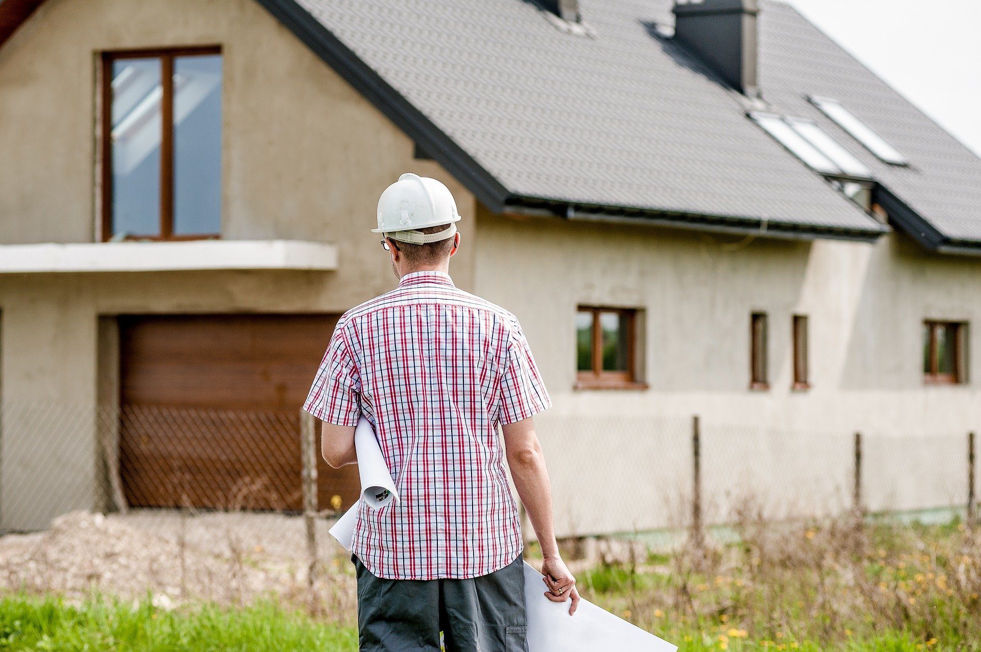 main in hard hat walking towards a house; How Not To Blow The Budget On Your House Building Project