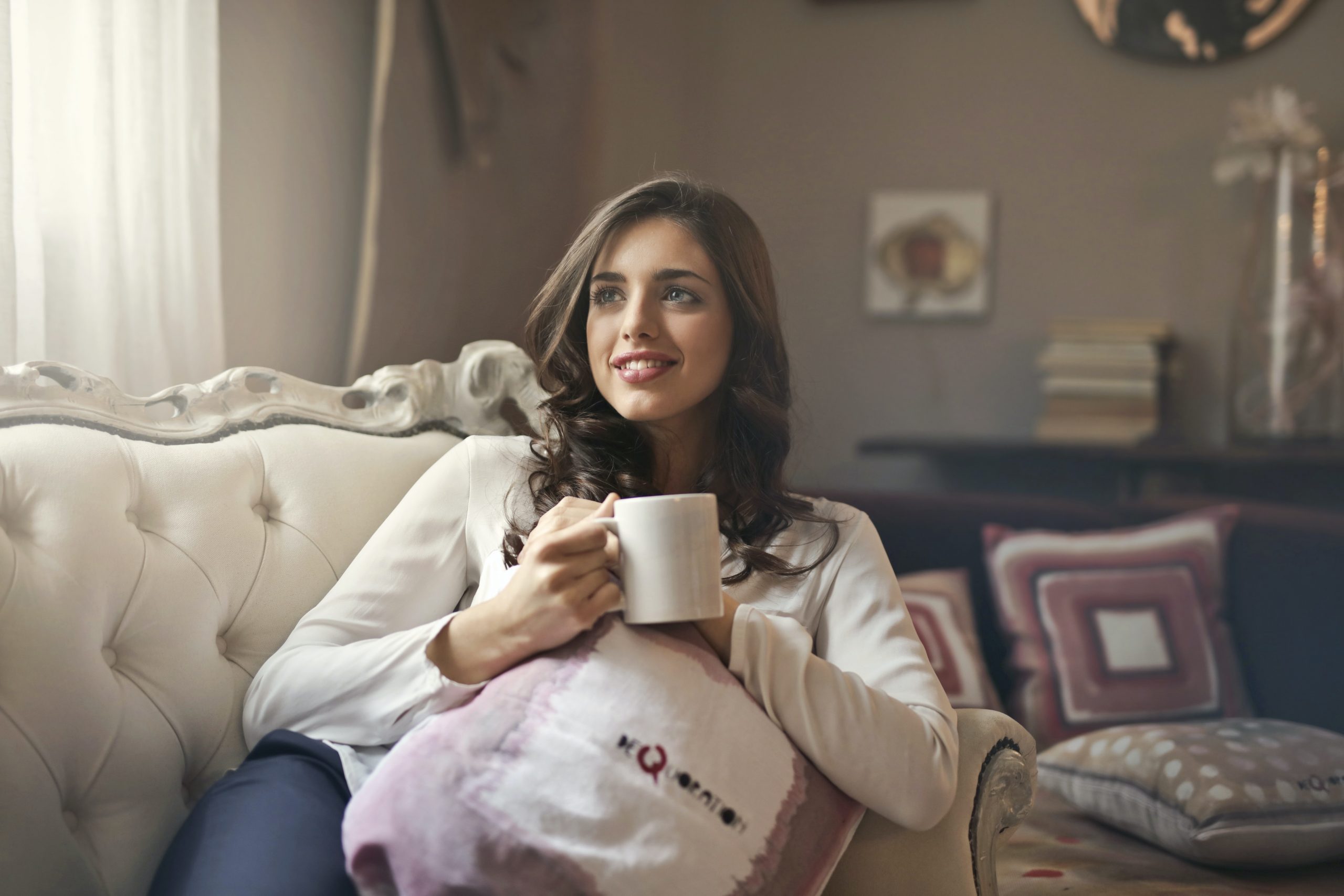 smiling dark haired woman laid on a sofa holding a mug; Make Sure Your Home Is Making You Happy With These Tips
