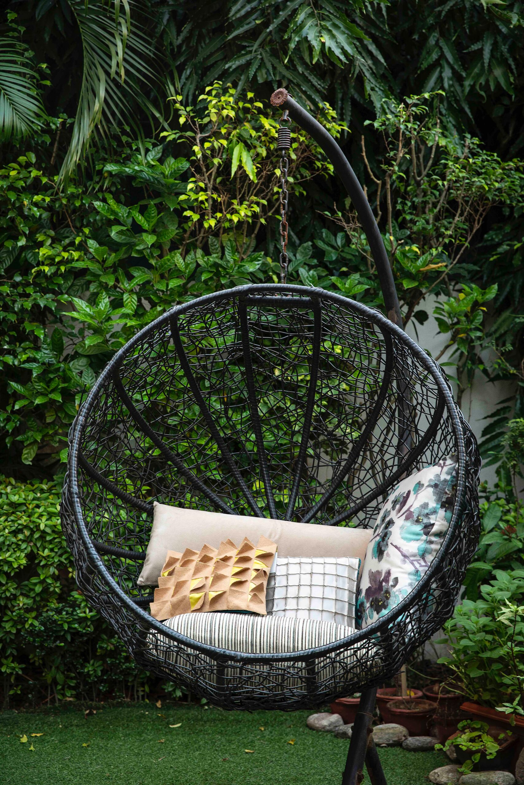 a black garden swing bubble style chair piled with various cushions; Simple Ways To Breathe New Life Into Your Backyard