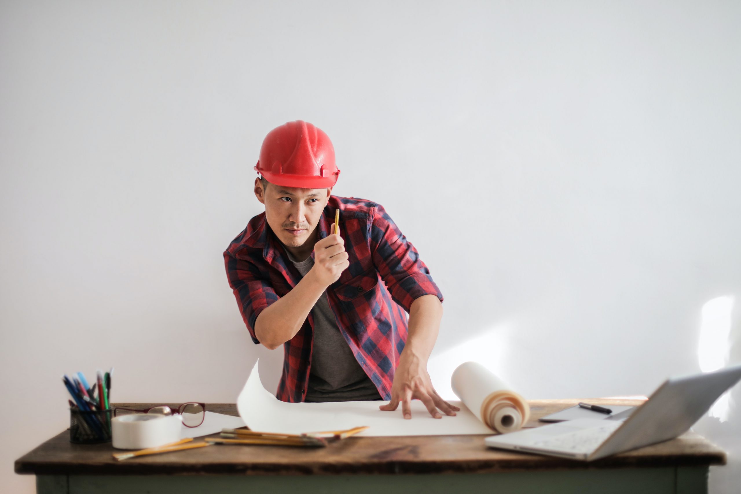 construction man wearing a red hard hat looking at a document; What Are The Biggest Fixer Upper Mistakes New Homeowners Make