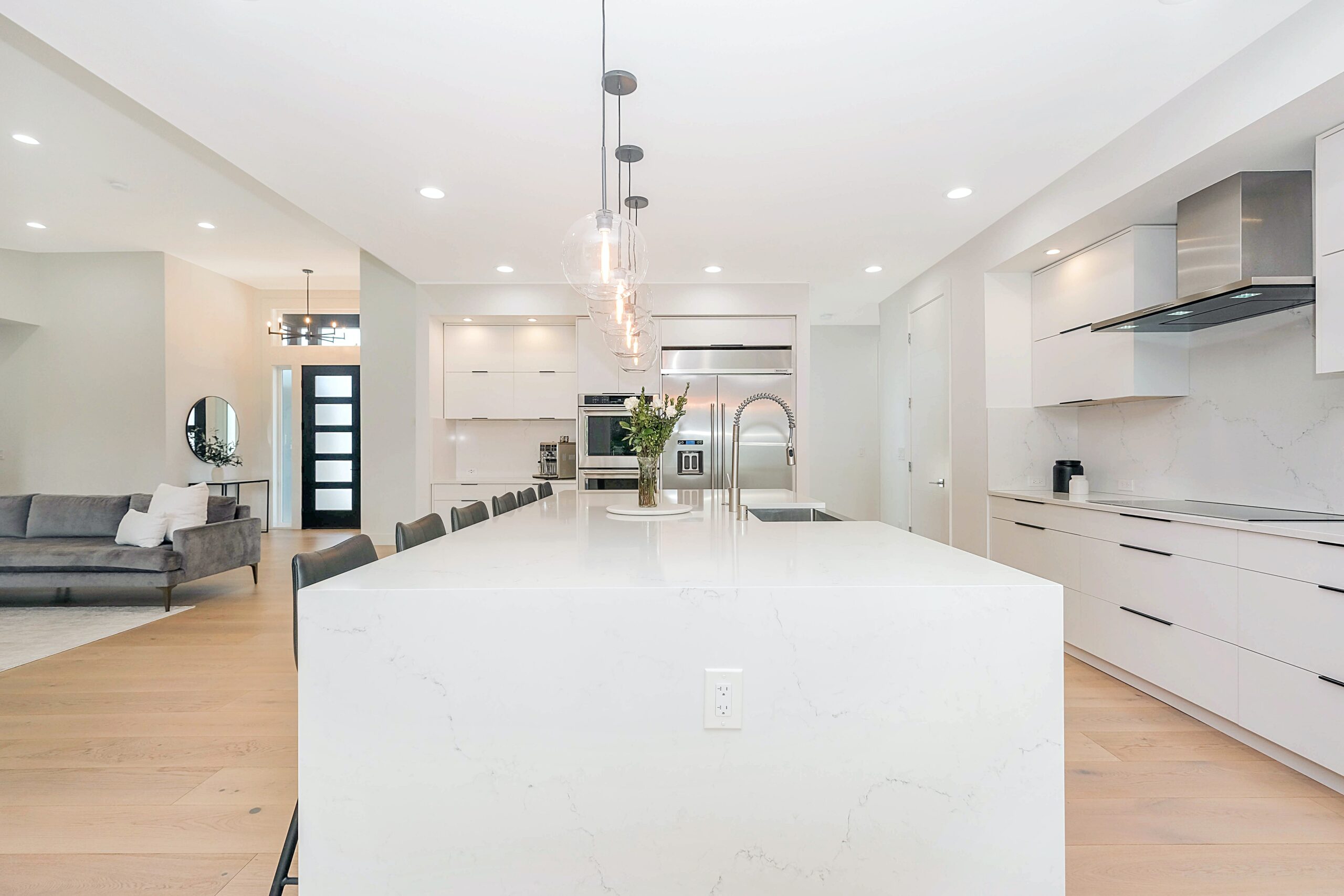 kitchen area with a large white kitchen island in the middle, with grey seating along one side of it and lights above it