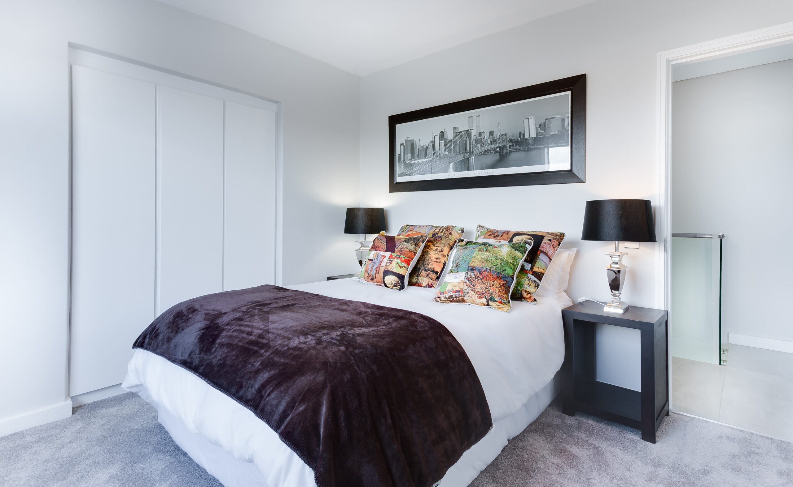 a large bed in a bedroom, with a long landscape photo on the wall above it and black lamps on the tables either side of the bed; Why More Thought Should Go Into Your Choice Of Bed
