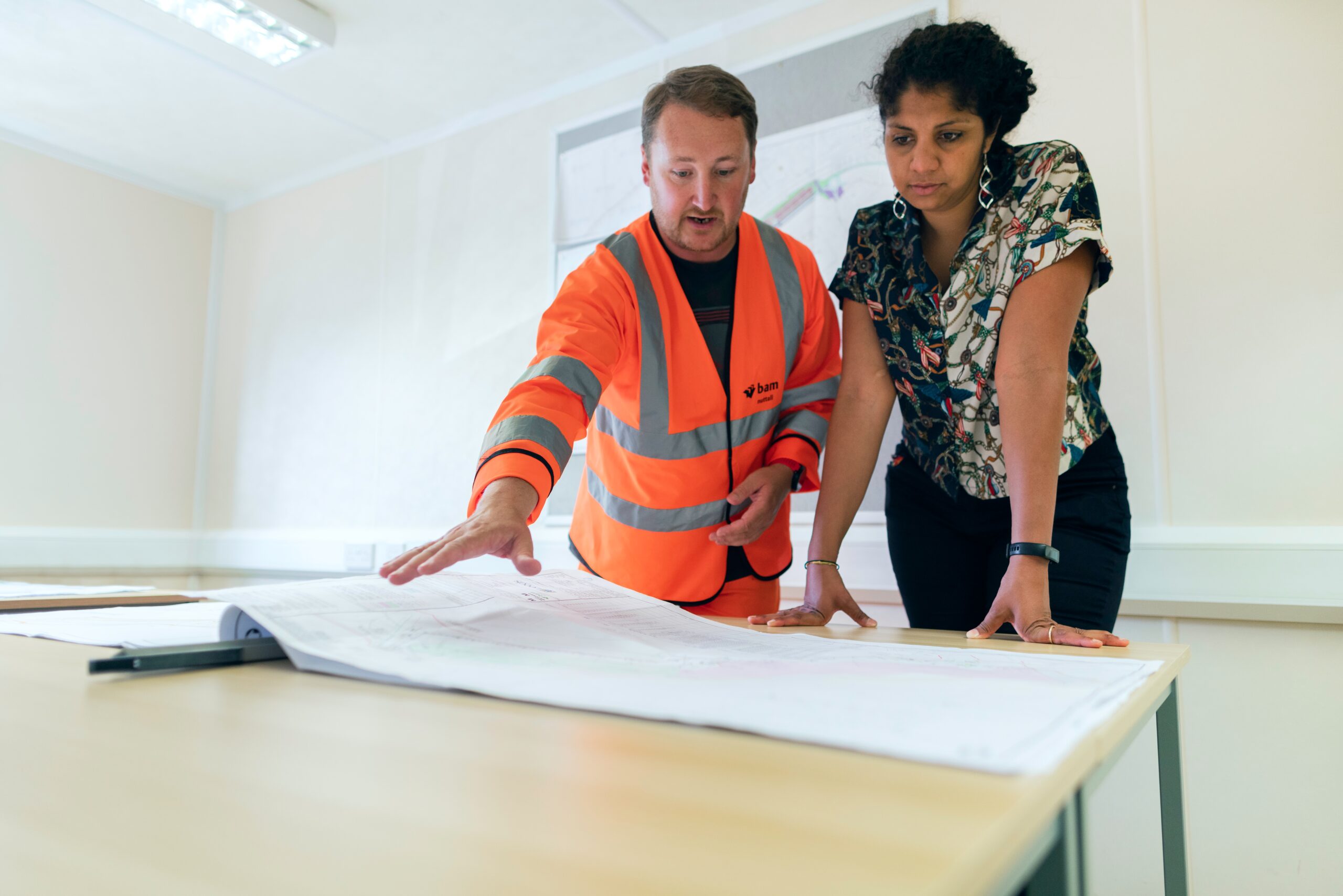 a male in a orange high visibility jacket, and a smartly dressed female, stood looking at a large sheet of paper; A Complete Guide to Property Maintenance for Real Estate Investors