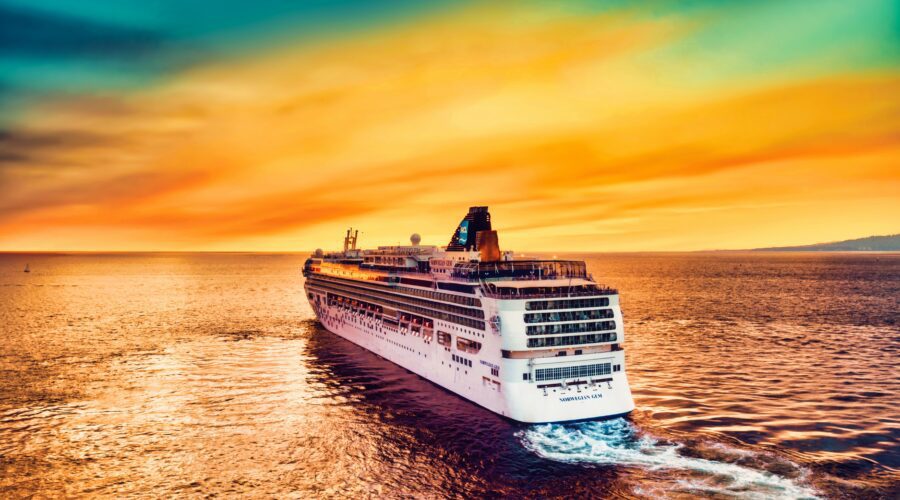 A photo of a large cruise ship taken from the air. It is taken at sunset so the sky is orange and blue with a golden glow on the sea