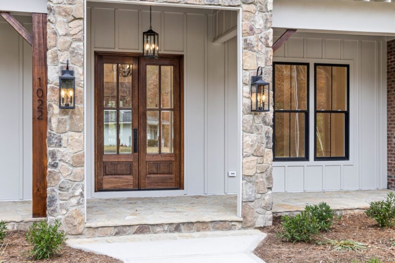 The exterior, porch, and entrance of a modern light coloured brick house. The door and windows are brown