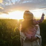 a photo of a mum holding a girl stood in a field in front of a sunset; The Great Outdoors - Encouraging a Love of Nature in Our Children