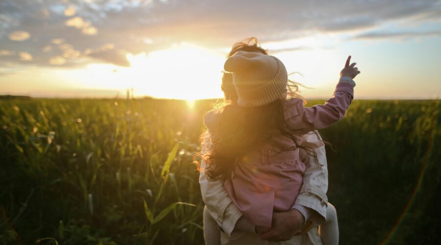 a photo of a mum holding a girl stood in a field in front of a sunset; The Great Outdoors - Encouraging a Love of Nature in Our Children