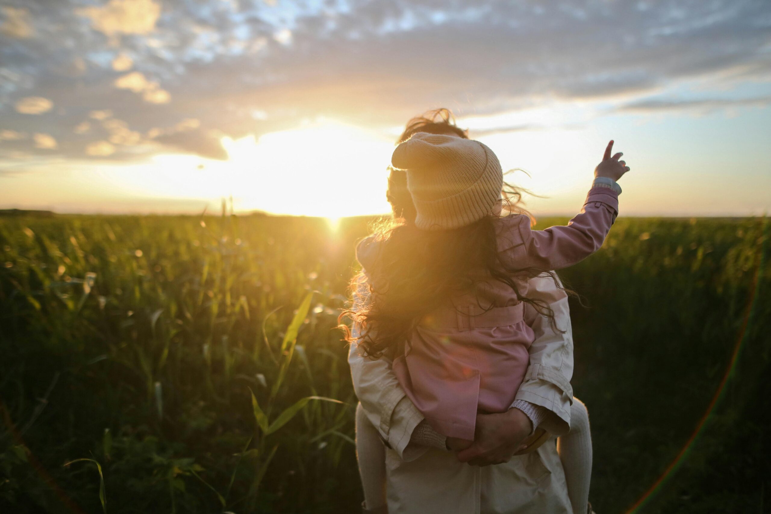 a photo of a mum holding a girl stood in a field in front of a sunset; The Great Outdoors - Encouraging a Love of Nature in Our Children