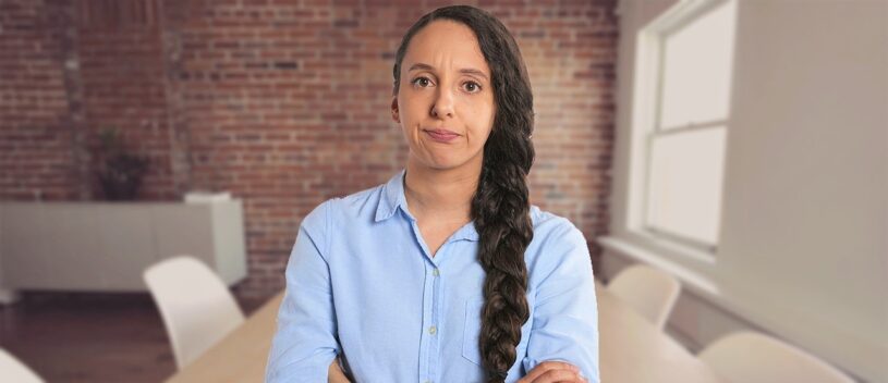A woman in a blue shirt with long plaited hair and arms crossed looking annoyed