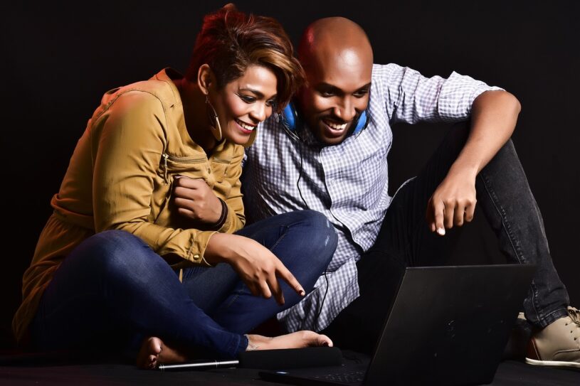 A man and a woman sat on the floor looking at a laptop while smiling