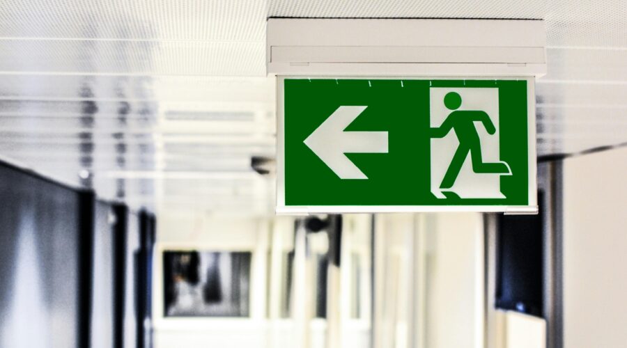 a corridor with a green safety sign - an arrow pointing right and a person running; Why You Can Never be Too Safety Conscious in Business