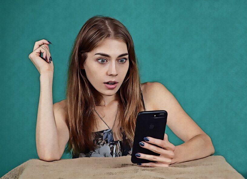A woman sat at a desk holding a cell phone looking surprised
