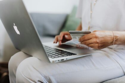 a person sat with a laptop on their knee and a credit card in their hand; A Quick Guide to Launching a Local E-Commerce Business
