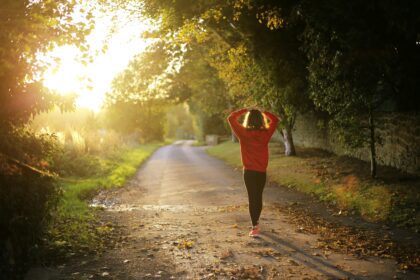 a woman photographed from behind, walking on a path through trees; How to Improve Your Health in Time for the New Year