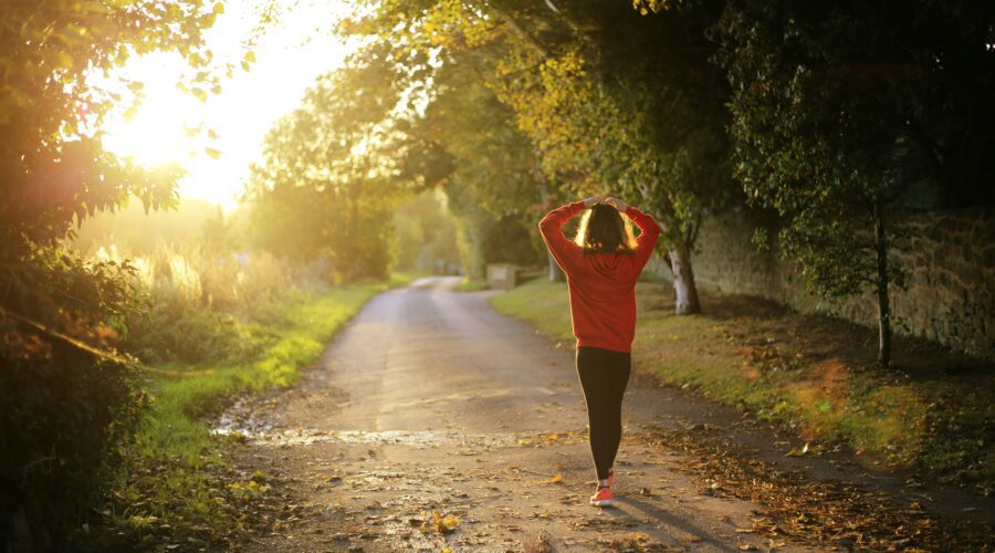 a woman photographed from behind, walking on a path through trees; How to Improve Your Health in Time for the New Year