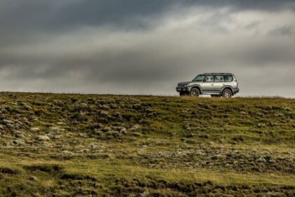 A simple green rugged landscape with a grey, cloudy sky. In the distance sits a silver 4x4 vehicle. Buying Your First 4x4 For Country Living