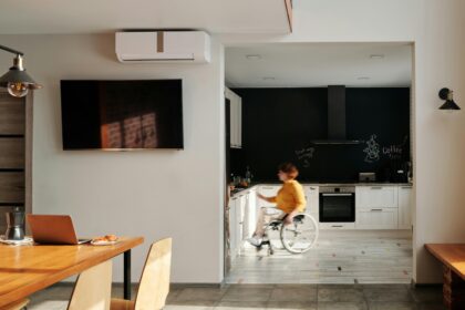 A landscape image of a kitchen in the distance with a person in a wheelchair showing that the kitchen has been modified for limited mobility; Finding the Right Tools for Better Mobility After an Injury