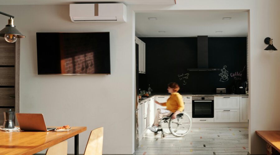 A landscape image of a kitchen in the distance with a person in a wheelchair showing that the kitchen has been modified for limited mobility; Finding the Right Tools for Better Mobility After an Injury