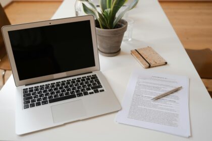 An open laptop is on the left of the screen. Behind the laptop is a small potted plant. Next to the laptop is a legal document with a pen resting on top; Why Planning Ahead Isn’t Pessimistic – It’s Empowering for Parents