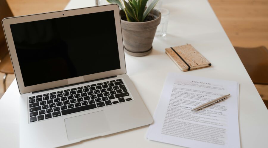 An open laptop is on the left of the screen. Behind the laptop is a small potted plant. Next to the laptop is a legal document with a pen resting on top; Why Planning Ahead Isn’t Pessimistic – It’s Empowering for Parents