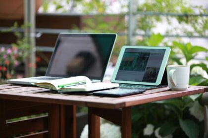 a brown desk surrounded by plants in a garden office, with two laptops on the desk; A New Look at How Garden Office Buildings Improve Everyday Productivity
