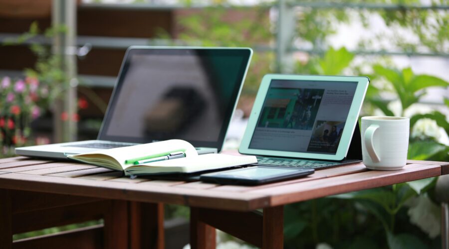 a brown desk surrounded by plants in a garden office, with two laptops on the desk; A New Look at How Garden Office Buildings Improve Everyday Productivity